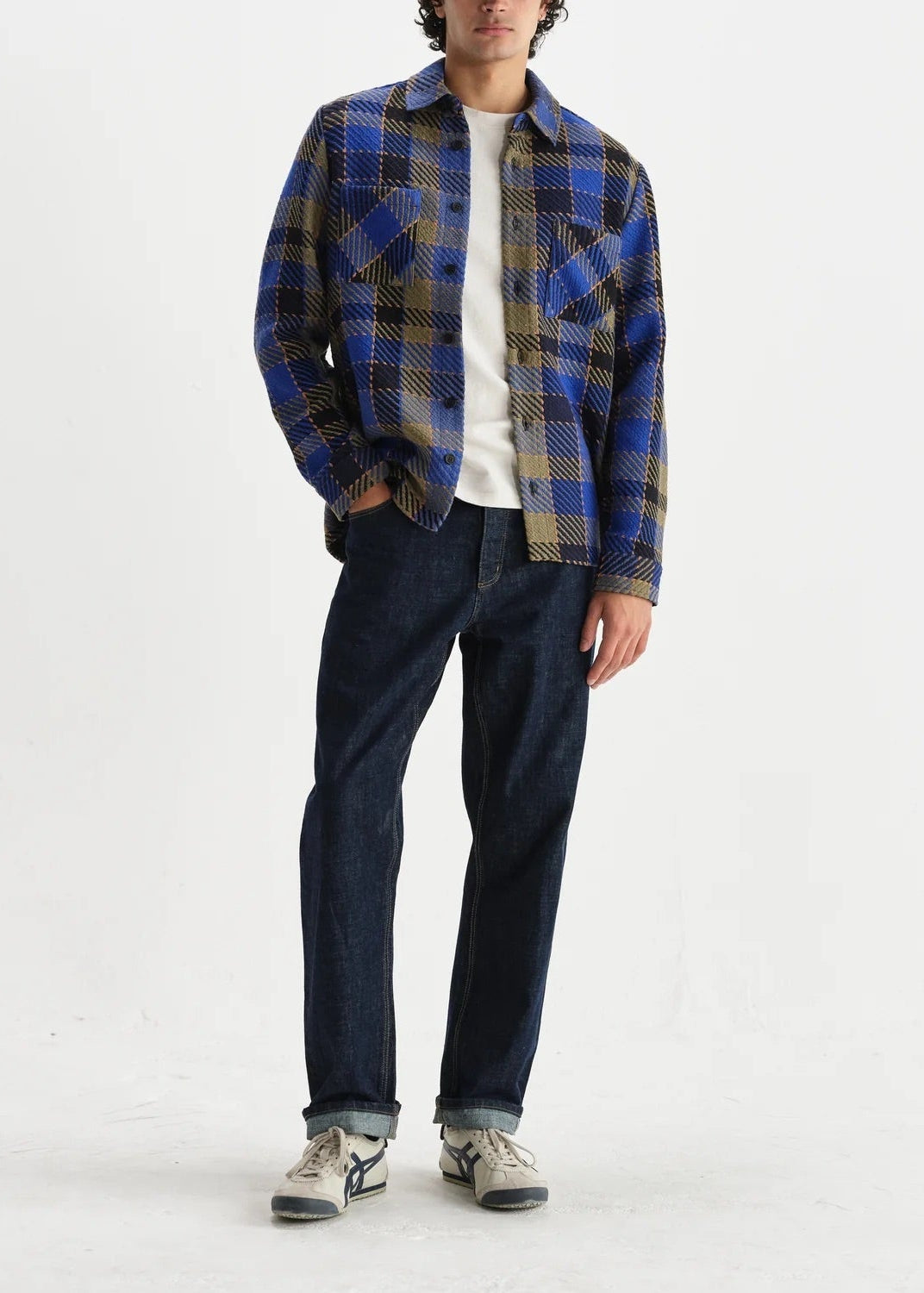 Person wearing a blue plaid shirt and dark jeans on a white background
