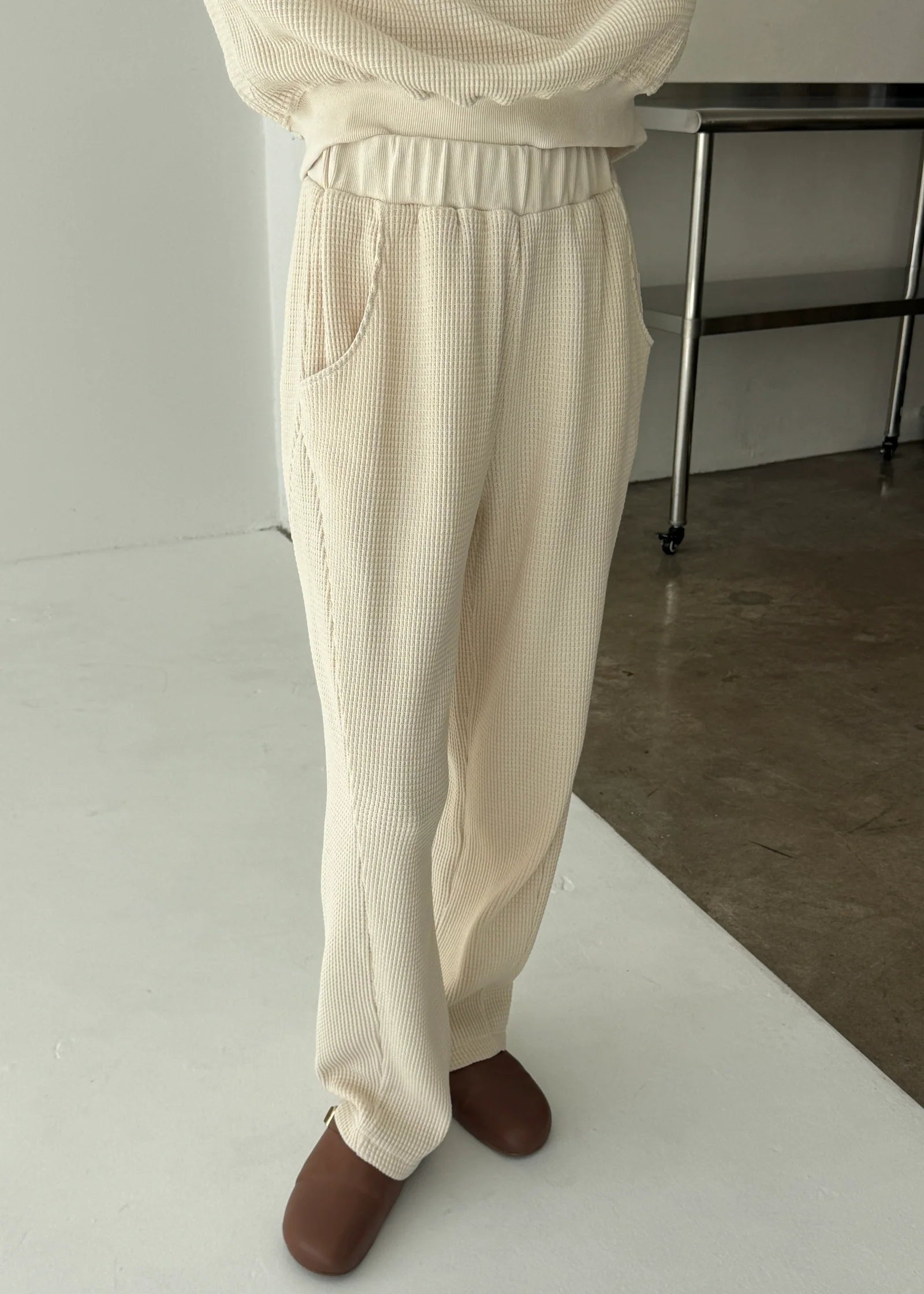 Person wearing beige corduroy pants and brown shoes on a white floor.