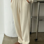 Person wearing a cream-colored outfit with wide-leg pants and brown shoes in a minimalistic setting.