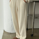 Person wearing a cream-colored outfit with wide-leg pants and brown shoes in a minimalistic setting.