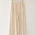 Beige pants hanging on a wooden hanger against a white wall