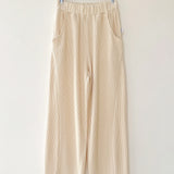Beige pants hanging on a wooden hanger against a white wall