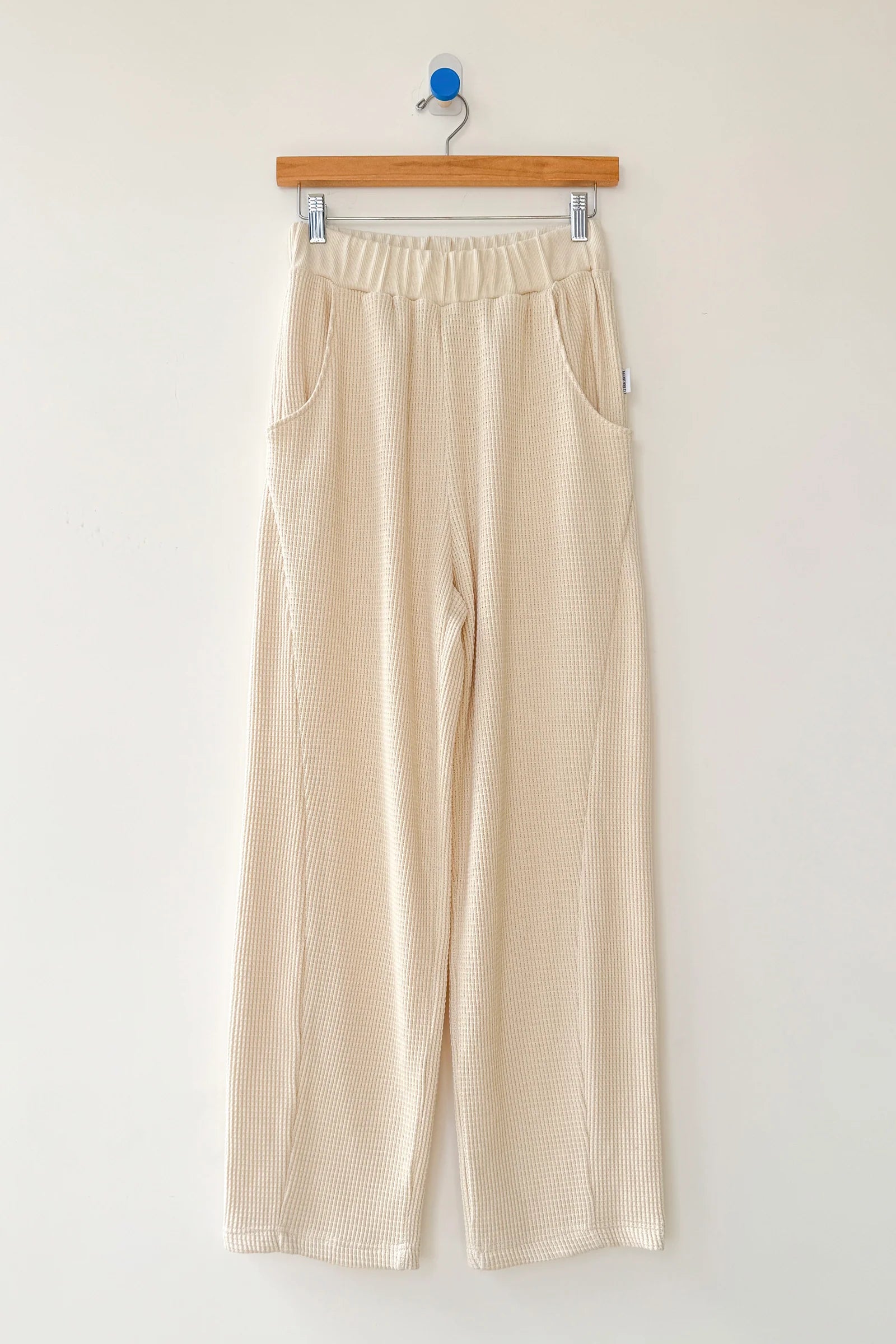 Beige pants hanging on a wooden hanger against a white wall