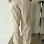 Person wearing beige ribbed pants and a matching top against a white wall.