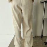 Person wearing beige ribbed pants and a matching top against a white wall.