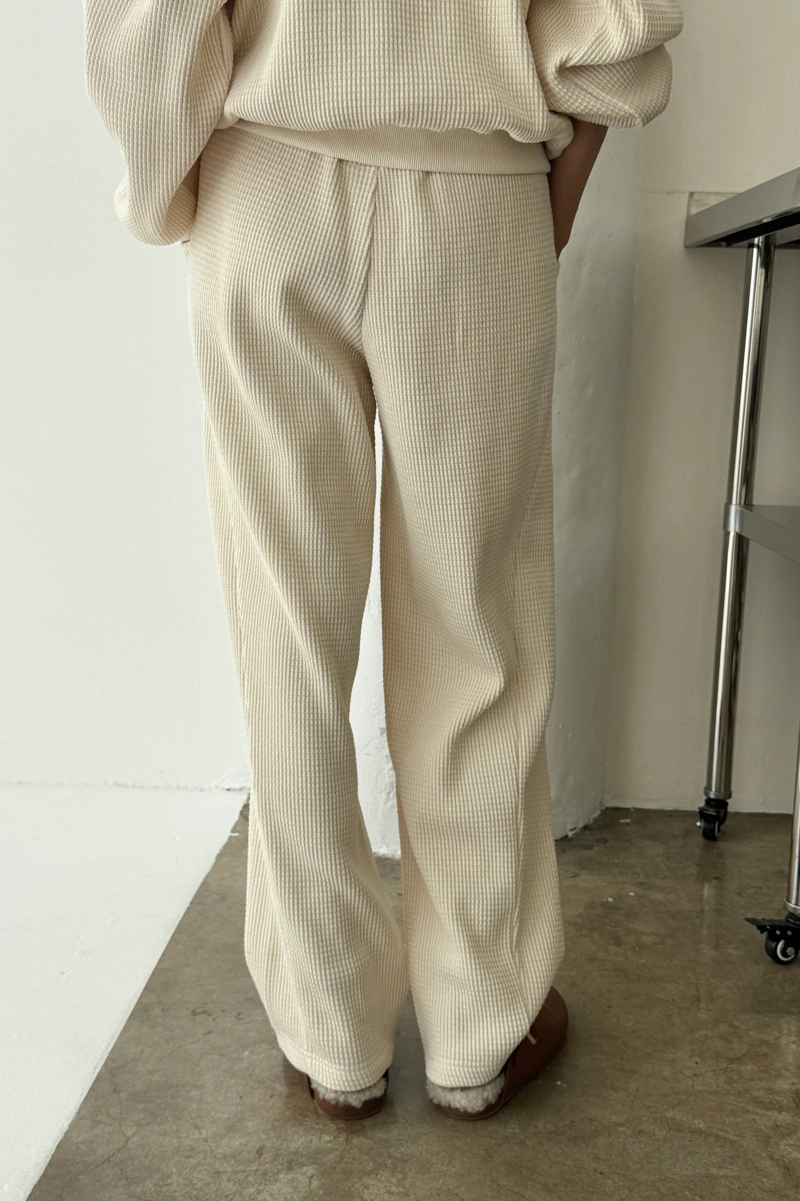 Person wearing beige ribbed pants and a matching top against a white wall.