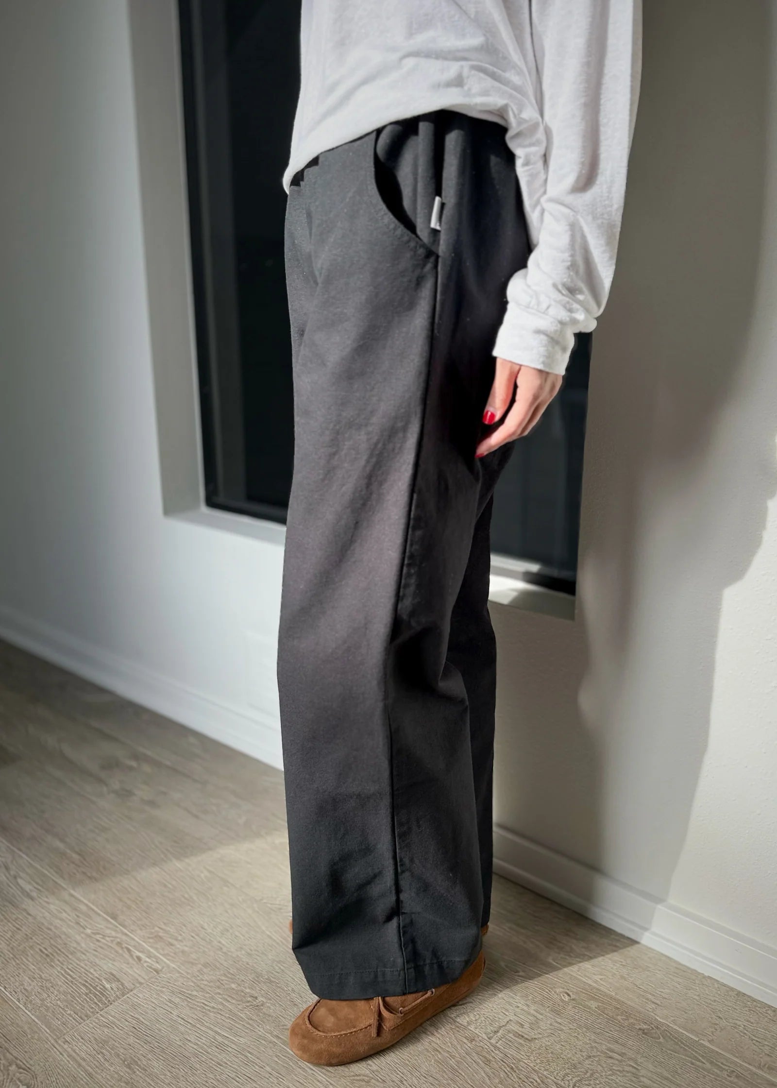 Person wearing gray pants and a white shirt standing in a room with a window.