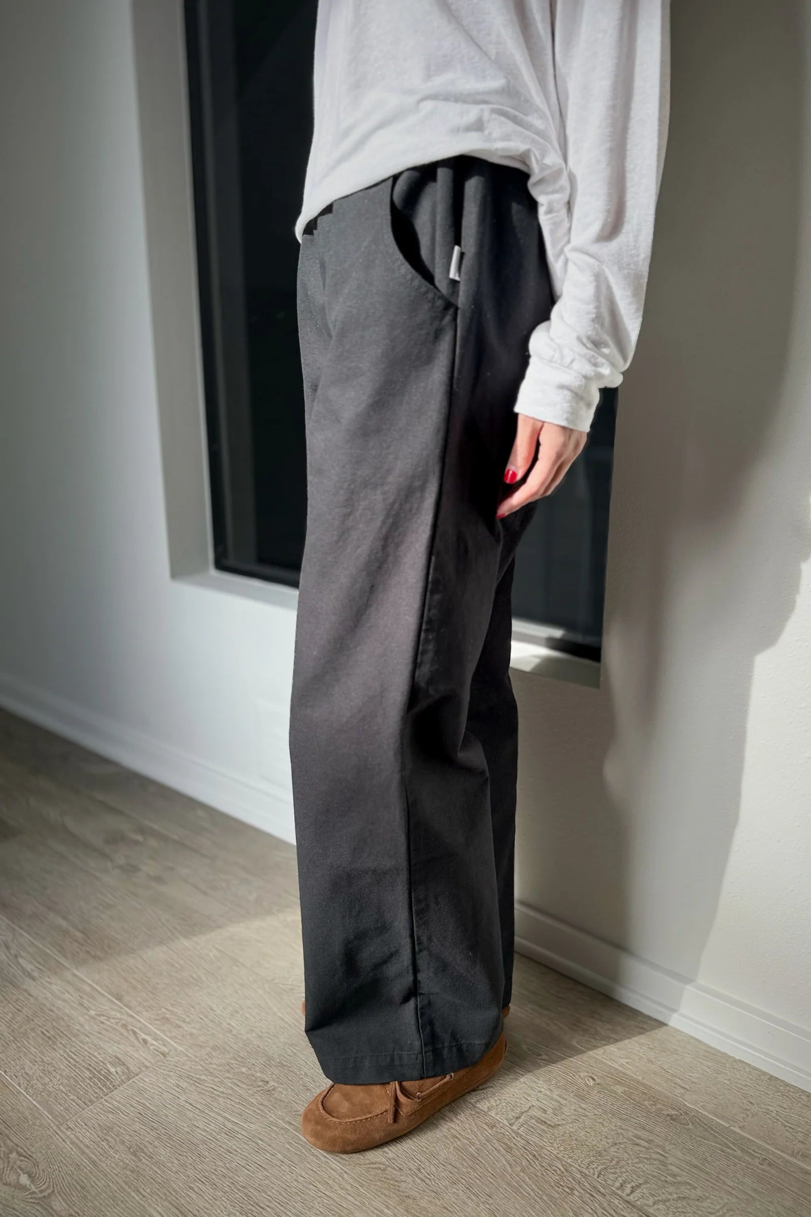 Person wearing gray pants and a white shirt standing in a room with a window.