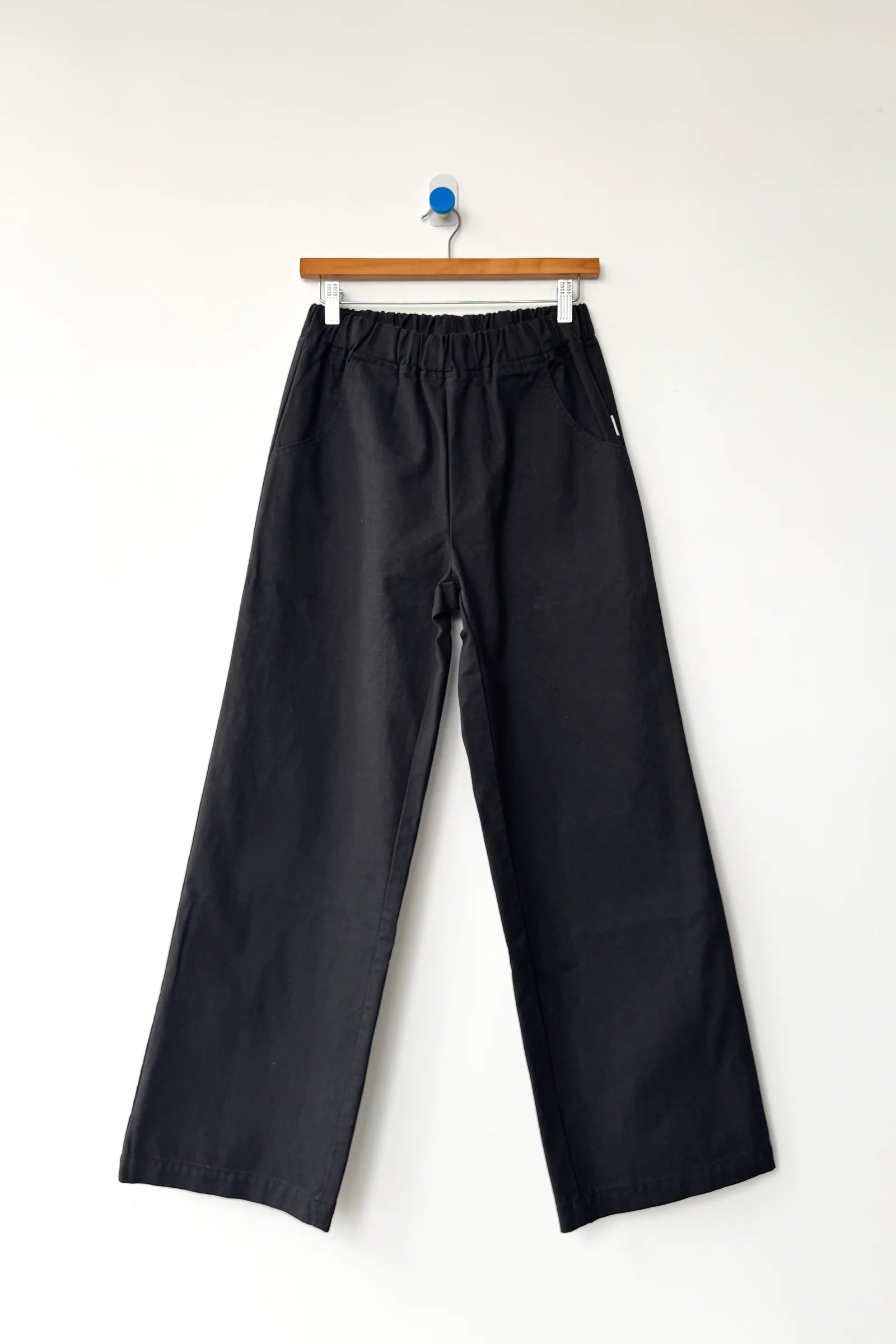 Black pants hanging on a wooden hanger against a white background