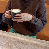 Person wearing a brown sweater holding a mug with a brick wall background