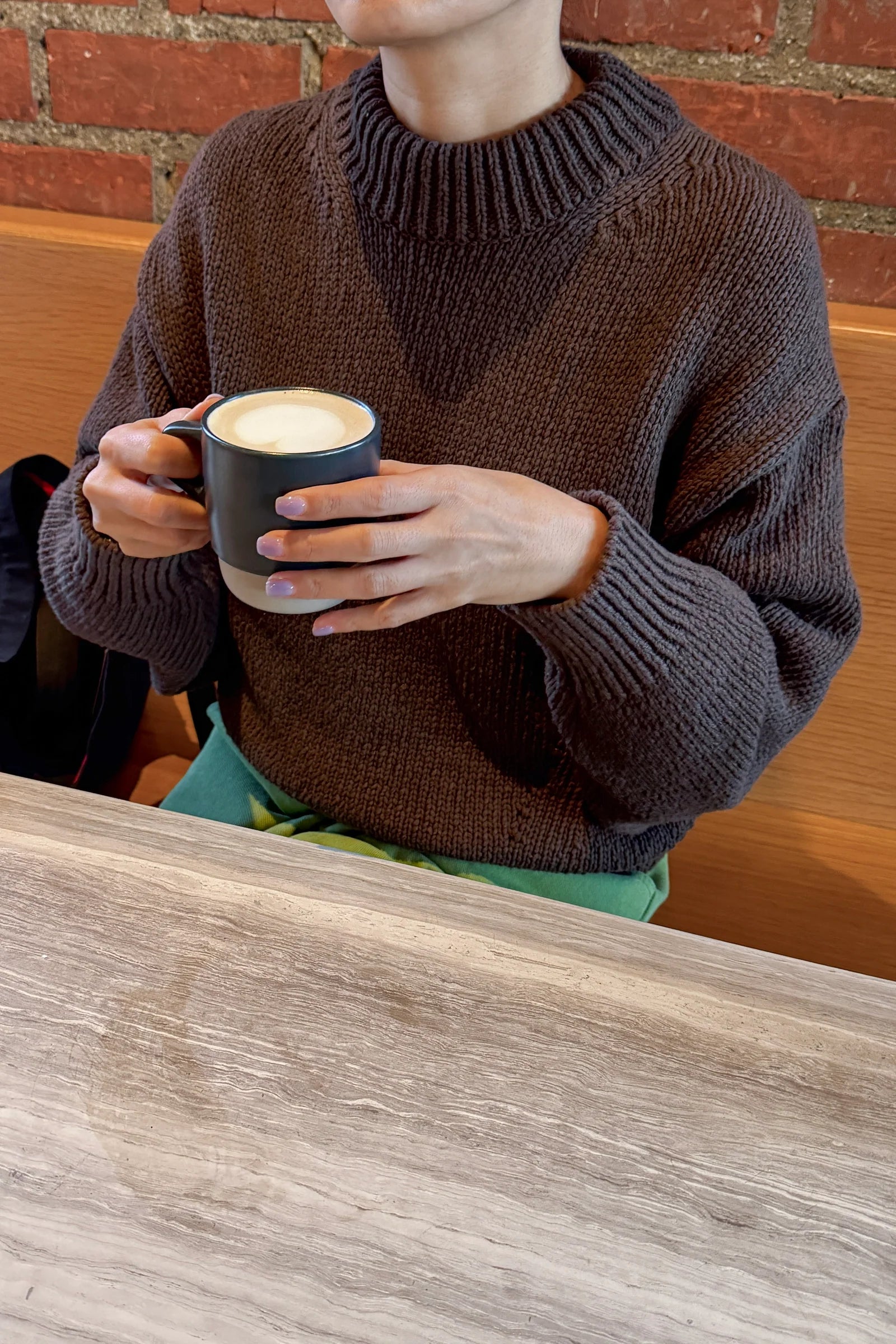 Person wearing a brown sweater holding a mug with a brick wall background