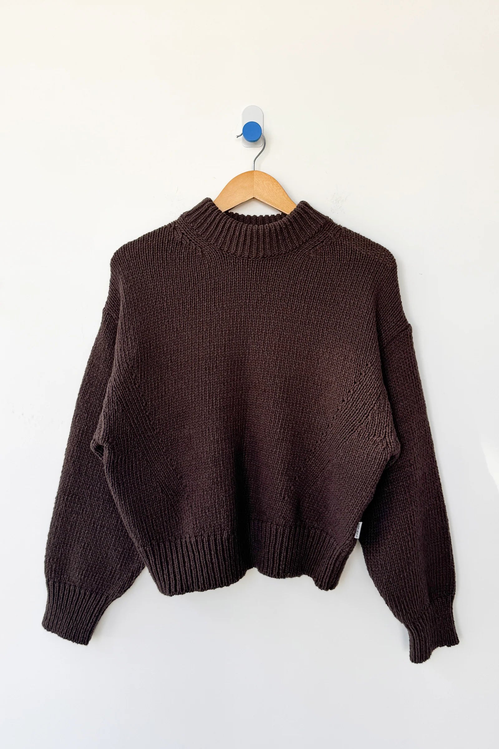 Brown sweater on a wooden hanger against a white background