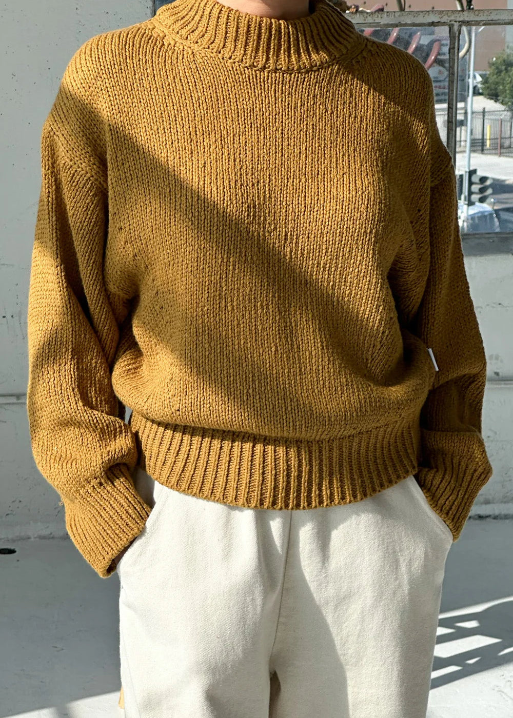 Person wearing a mustard yellow sweater and white pants outdoors.