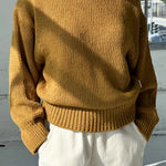 Person wearing a mustard yellow sweater and white pants outdoors.