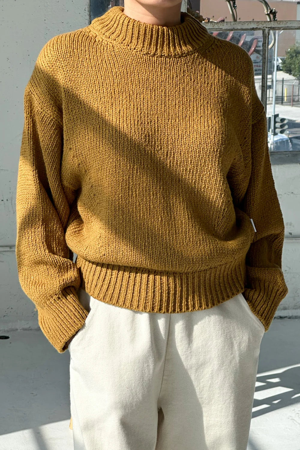 Person wearing a mustard yellow sweater and white pants outdoors.