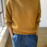 Person wearing a mustard yellow sweater and blue jeans indoors.