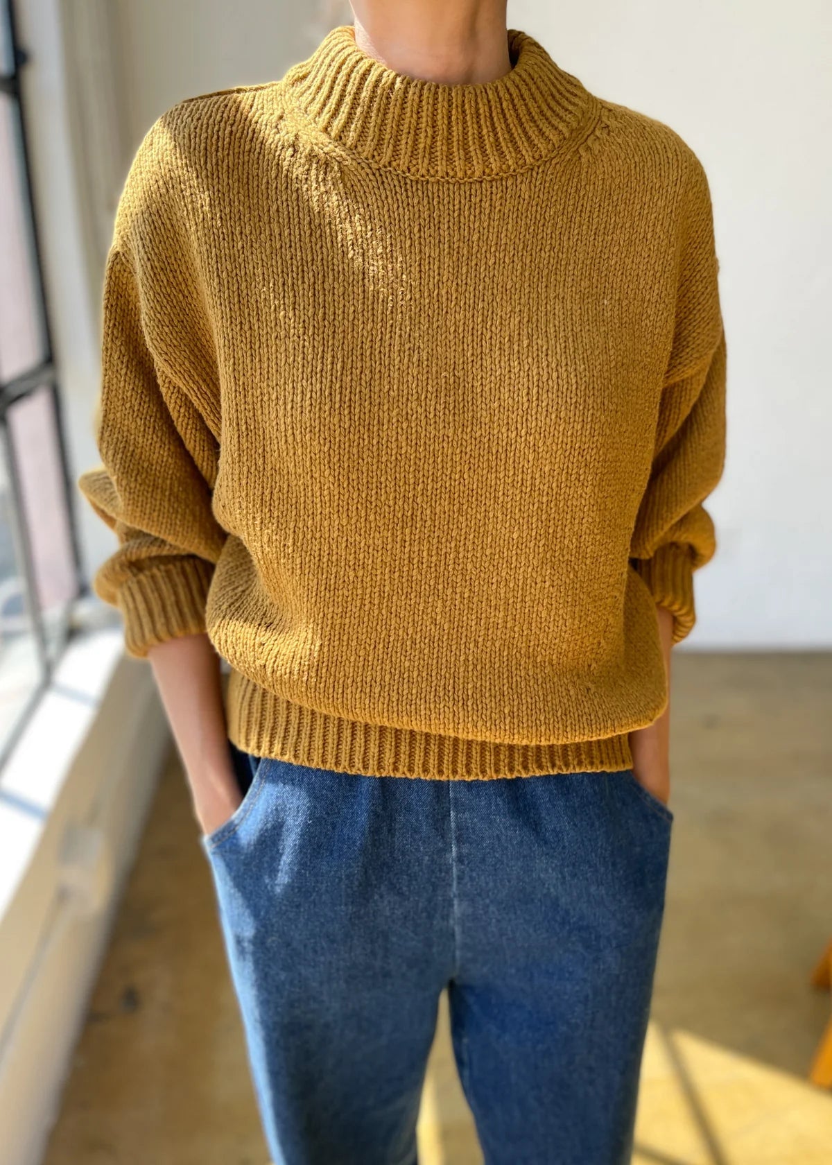 Person wearing a mustard yellow sweater and blue jeans indoors.