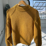 Yellow sweater on a hanger against a light-colored wall with a window in the background.