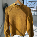 Yellow sweater on a hanger against a light-colored wall with a window in the background.