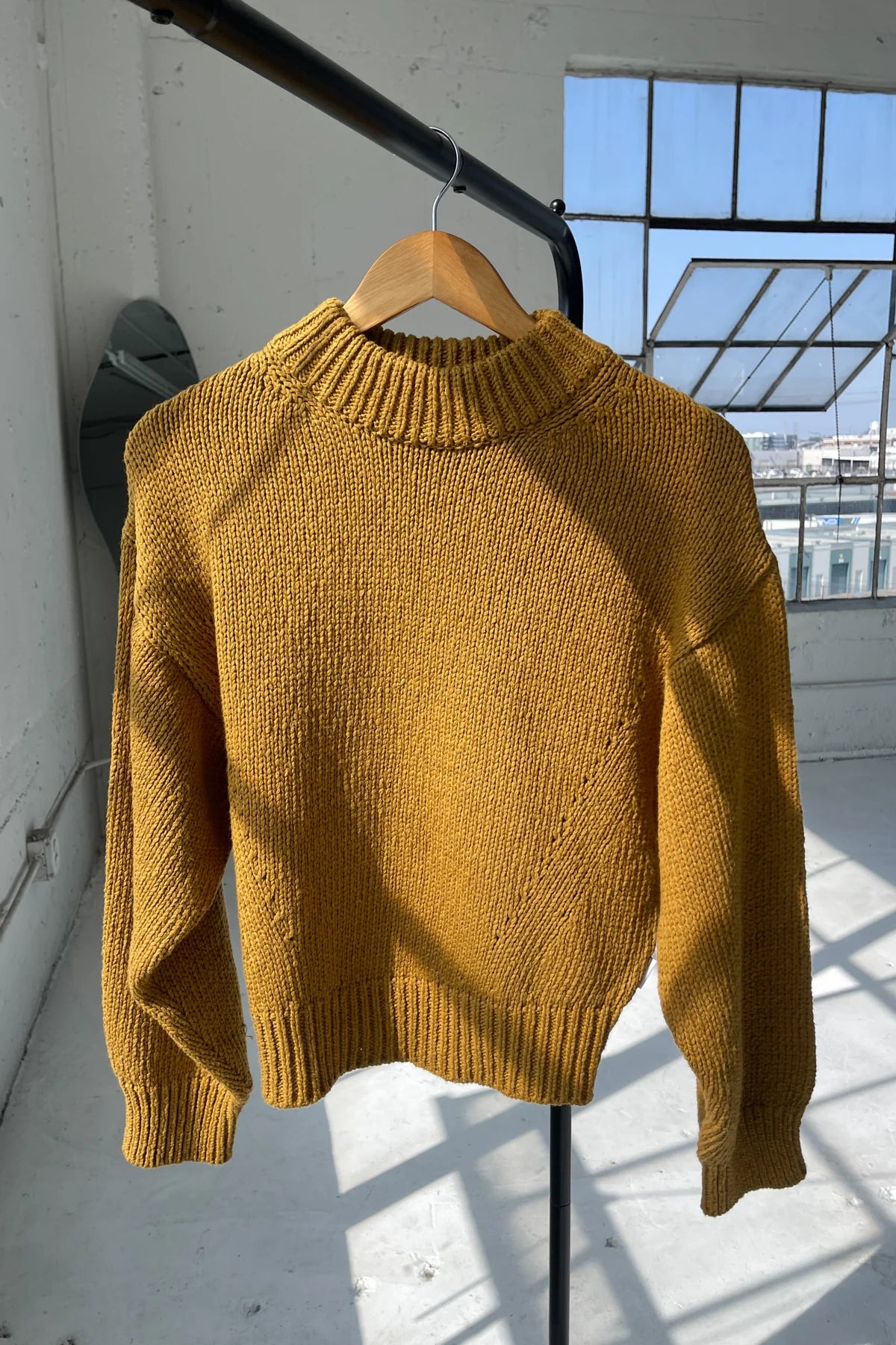 Yellow sweater on a hanger against a light-colored wall with a window in the background.