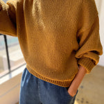 Person wearing a mustard yellow sweater and blue jeans indoors.