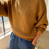 Person wearing a mustard yellow sweater and blue jeans indoors.
