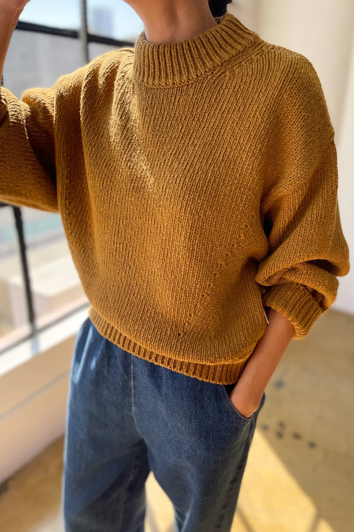 Person wearing a mustard yellow sweater and blue jeans indoors.