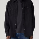 Person wearing a black button-up shirt over a black t-shirt with blue jeans on a white background