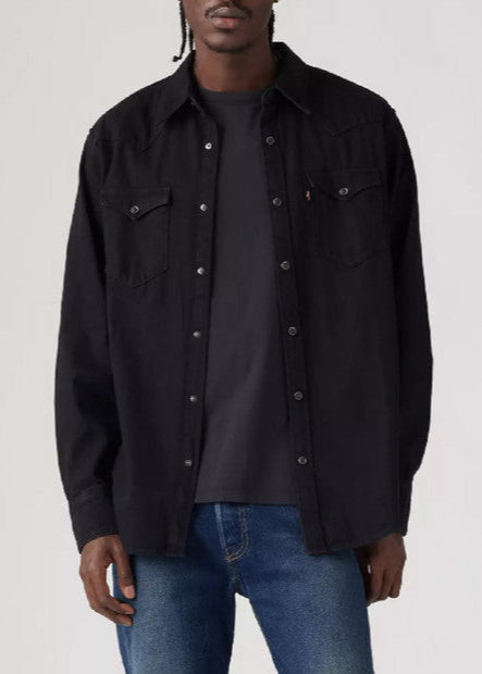 Person wearing a black button-up shirt over a black t-shirt with blue jeans on a white background
