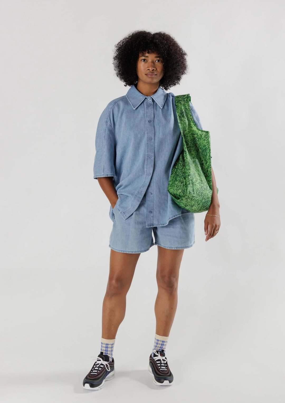 Women wearing a denim shirt and shorts and holding a green grass printed tote bag
