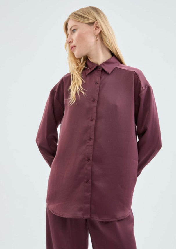 A medium close image of a female model posing in the Eggplant Satin Shirt styled with matching pants