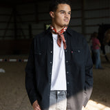 Man wearing a black jacket, white shirt, and patterned scarf in an indoor setting