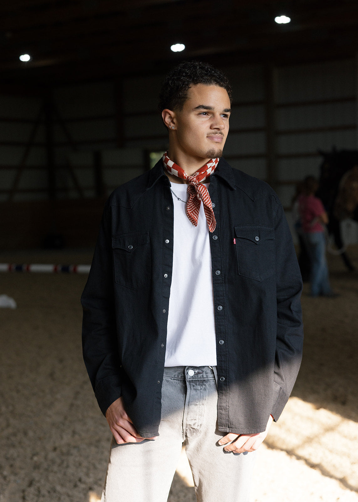 Man wearing a black jacket, white shirt, and patterned scarf in an indoor setting