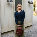 Woman standing outside a wooden building holding a brown backpack