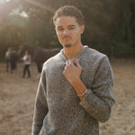 Man wearing a gray sweater standing outdoors with trees in the background