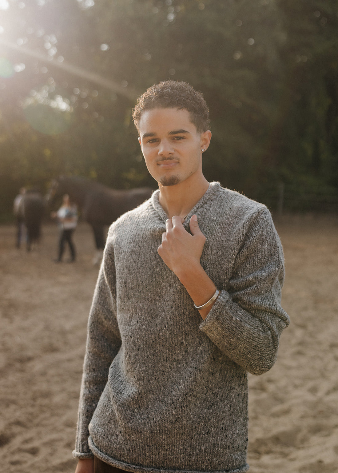 Man wearing a gray sweater standing outdoors with trees in the background
