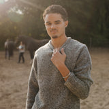 Man wearing a gray sweater standing outdoors with trees in the background