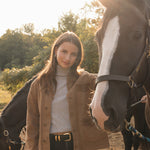 Woman standing with a horse in an outdoor setting with trees and a barn in the background