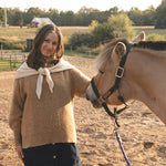 Woman standing next to a horse in an outdoor setting with trees and fields in the background.