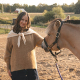 Woman standing next to a horse in an outdoor setting with trees and fields in the background.