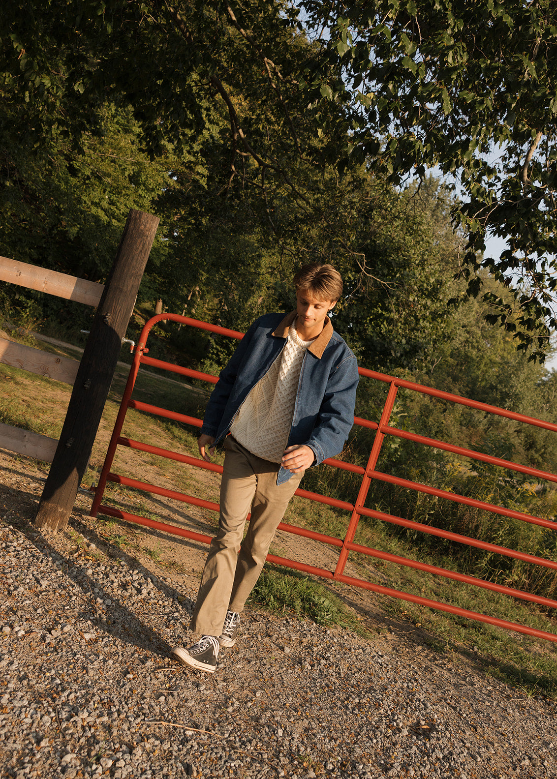 Man standing near a red metal gate with trees in the background