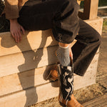 Person wearing cowboy boots and a tan jacket sitting on a wooden structure.
