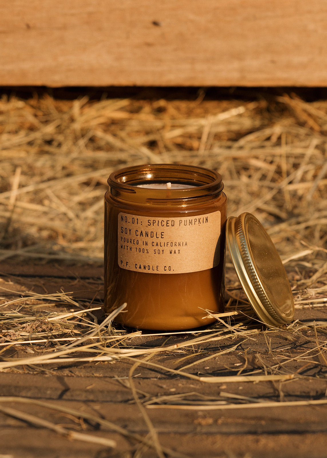 Spiced pumpkin candle in a jar with a label on straw and wooden background