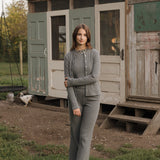 Woman in a gray outfit standing in front of a rustic wooden shed with chickens in the background.