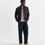 Man wearing a plaid shirt, white t-shirt, and dark jeans on a white background