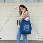 Women model holding a denim tote with a sketch of the Frances Jaye store front on it.