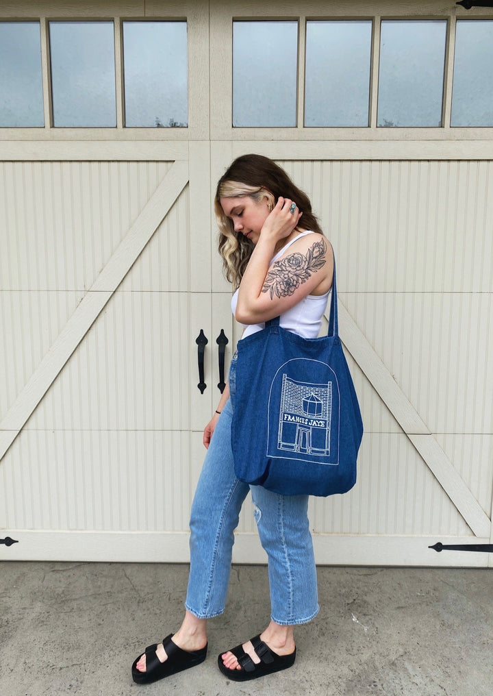 Women model holding a denim tote with a sketch of the Frances Jaye store front on it.