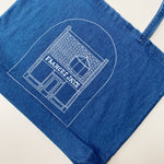 Women model holding a denim tote with a sketch of the Frances Jaye store front on it.