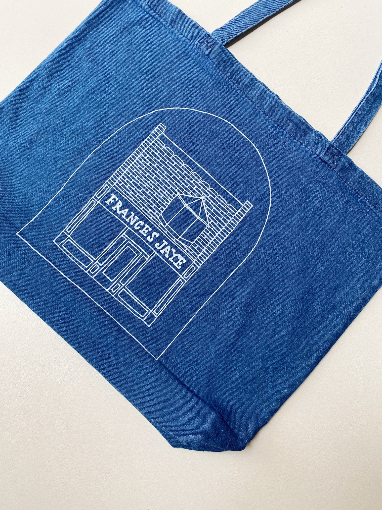 Women model holding a denim tote with a sketch of the Frances Jaye store front on it.