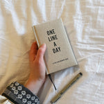 One Line a Day journal laying on a bed with a pen.
